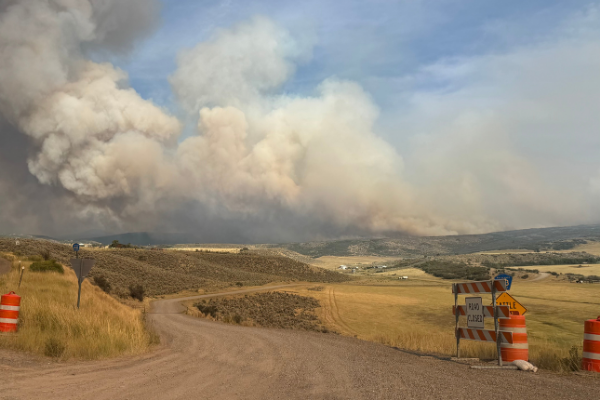 Image of a dirt road winding through the mountains with a smoke plume in the distance