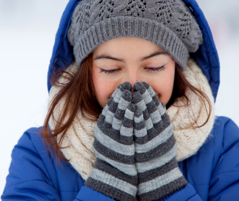 Person who is outside and dressed up in winter gear with mittens held up to her face